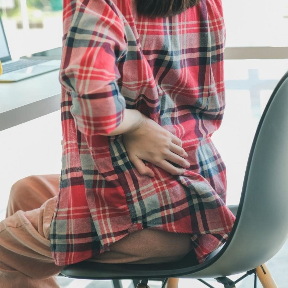 photo of person sitting at a desk while holding their back because of sciatica